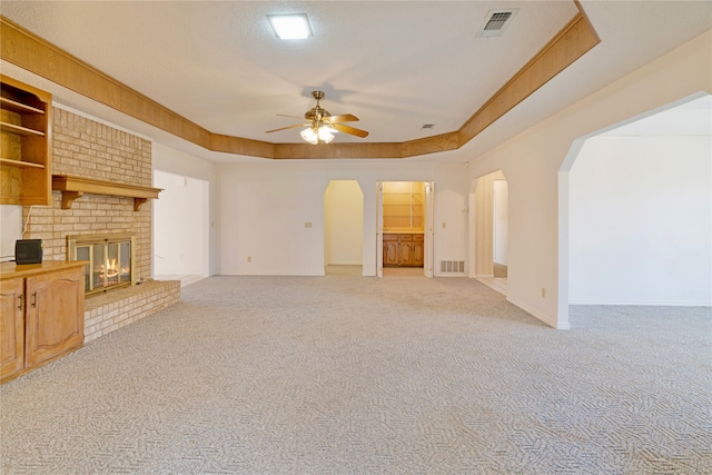 unfurnished living room with a raised ceiling, a brick fireplace, visible vents, and arched walkways