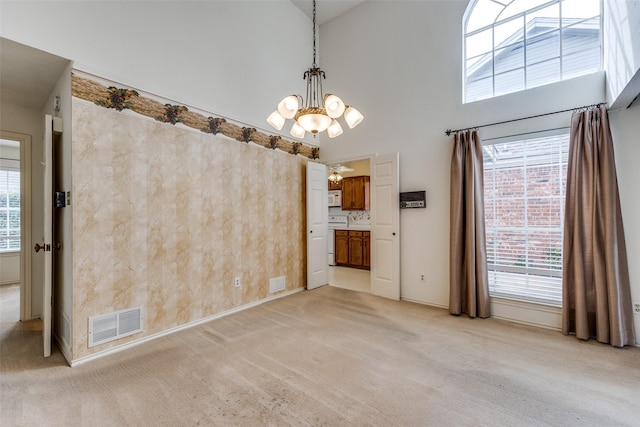 unfurnished dining area featuring light carpet, visible vents, an inviting chandelier, and a towering ceiling