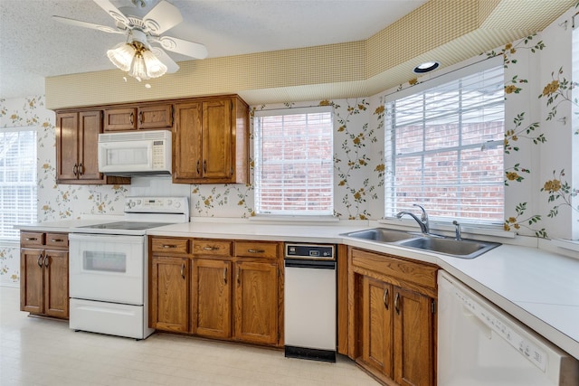 kitchen featuring wallpapered walls, white appliances, brown cabinetry, and a sink