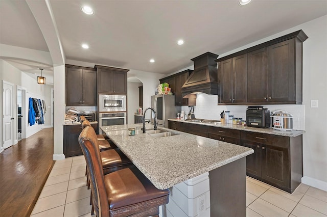 kitchen featuring custom range hood, a sink, arched walkways, dark brown cabinetry, and appliances with stainless steel finishes