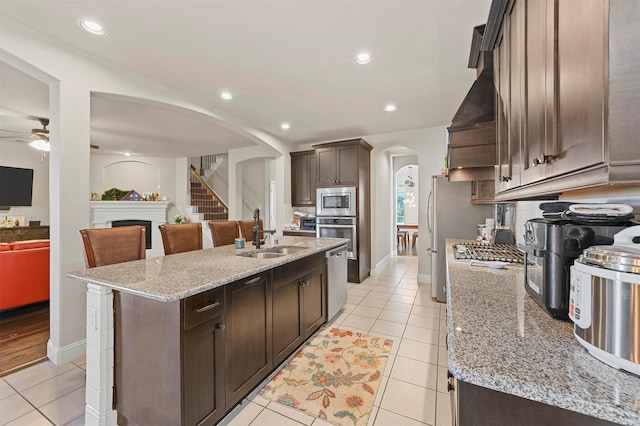 kitchen with light tile patterned floors, arched walkways, stainless steel appliances, a sink, and dark brown cabinets