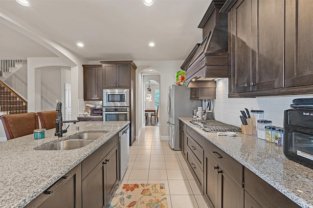 kitchen with a sink, stainless steel appliances, arched walkways, light tile patterned flooring, and dark brown cabinets