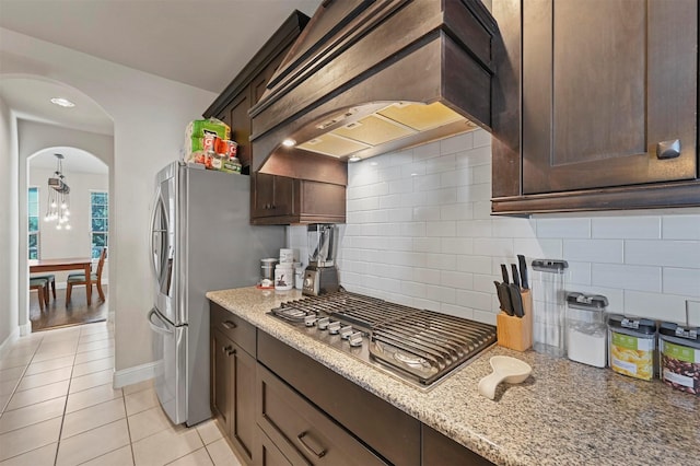 kitchen with dark brown cabinetry, tasteful backsplash, premium range hood, and stainless steel appliances