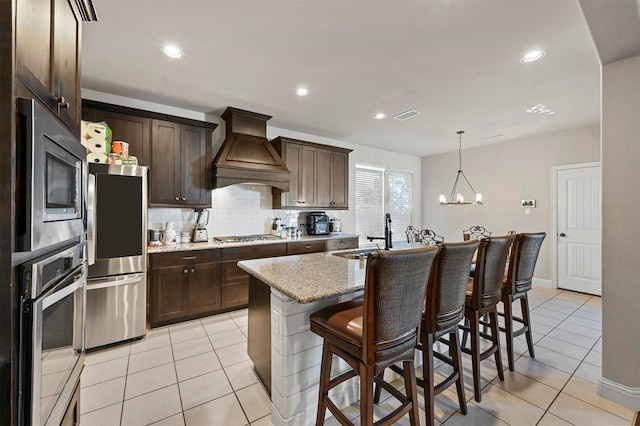 kitchen with custom exhaust hood, appliances with stainless steel finishes, light tile patterned flooring, and a sink