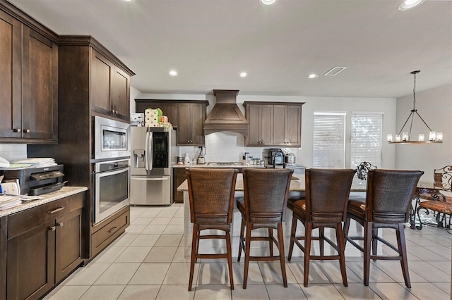 kitchen with a breakfast bar, custom range hood, stainless steel appliances, decorative backsplash, and dark brown cabinets