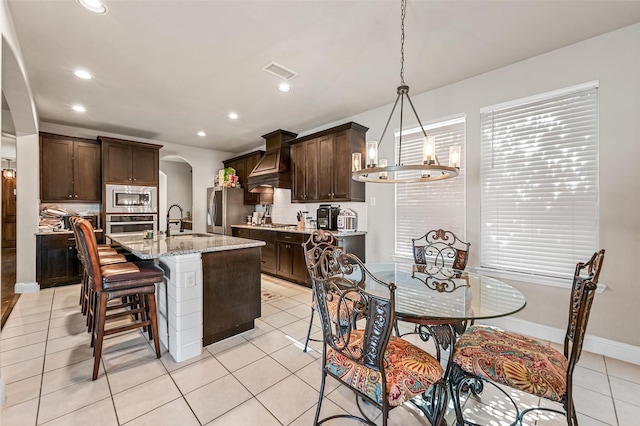 kitchen featuring visible vents, arched walkways, dark brown cabinetry, appliances with stainless steel finishes, and custom exhaust hood