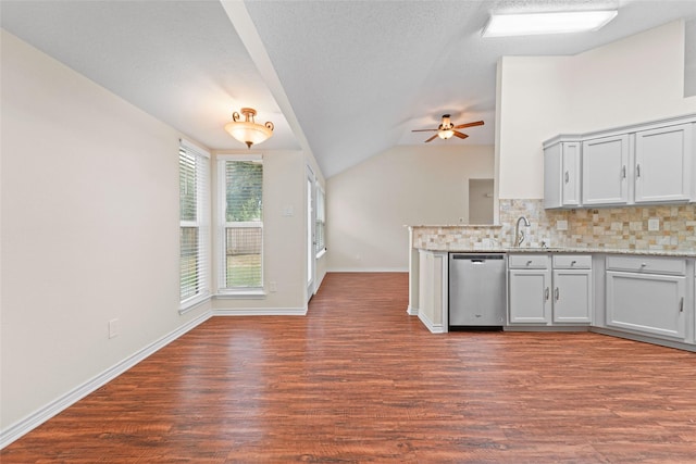 kitchen with dark wood finished floors, a peninsula, vaulted ceiling, stainless steel dishwasher, and backsplash