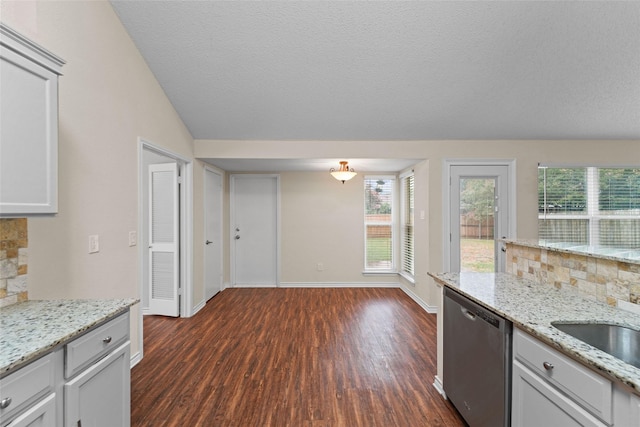 kitchen featuring backsplash, lofted ceiling, light stone counters, stainless steel dishwasher, and dark wood-style flooring