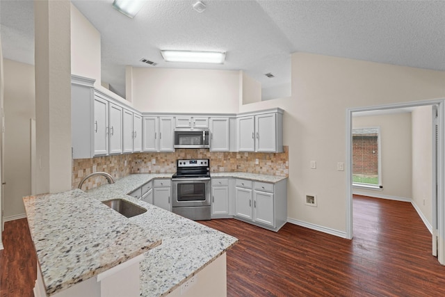 kitchen featuring vaulted ceiling, light stone counters, appliances with stainless steel finishes, a peninsula, and a sink