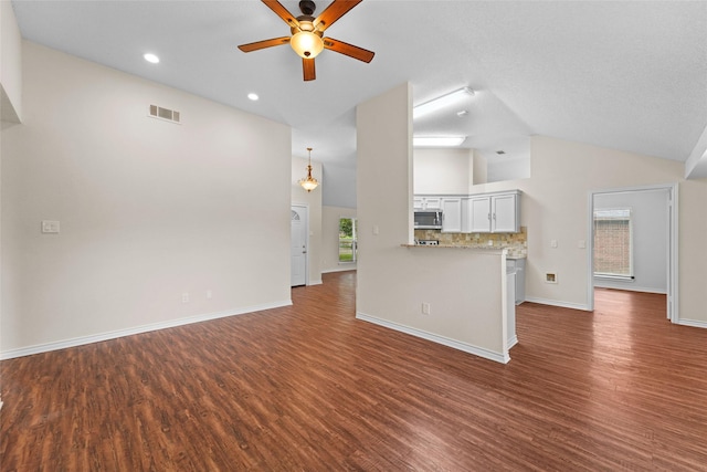 unfurnished living room featuring visible vents, baseboards, ceiling fan, vaulted ceiling, and dark wood-style flooring