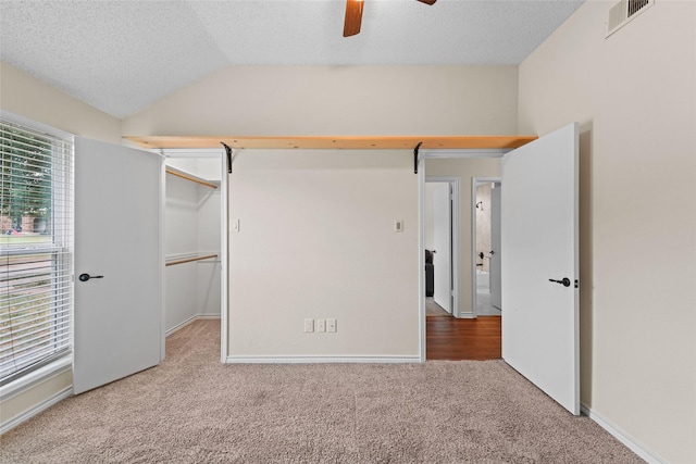 unfurnished bedroom featuring lofted ceiling, carpet flooring, visible vents, and a textured ceiling