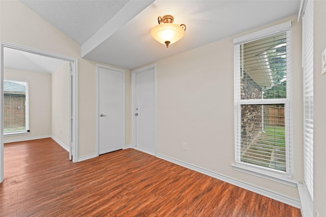 unfurnished bedroom with a textured ceiling, lofted ceiling, baseboards, and wood finished floors