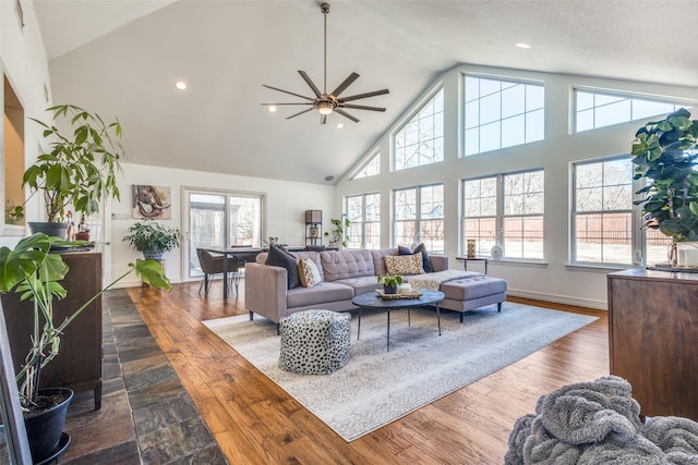 living room with a wealth of natural light, a ceiling fan, dark wood-type flooring, and high vaulted ceiling