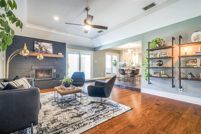 living area featuring wood finished floors, crown molding, a fireplace, and visible vents