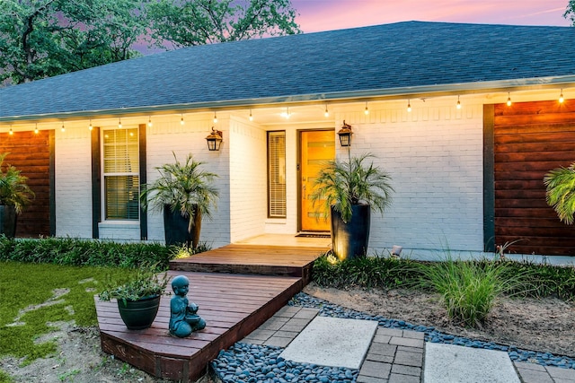 property entrance featuring brick siding and roof with shingles