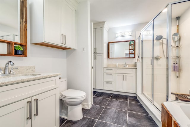 bathroom with a stall shower, toilet, two vanities, and a sink