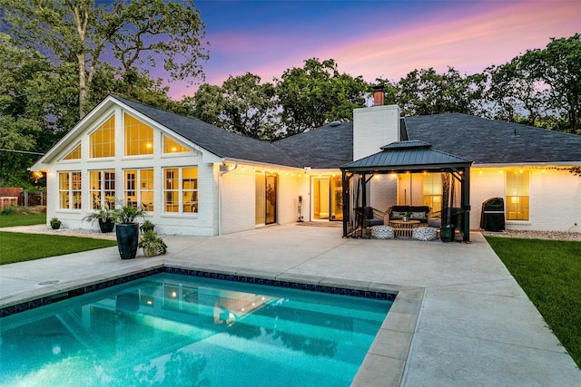 back of house at dusk with a gazebo, a chimney, brick siding, and an outdoor living space