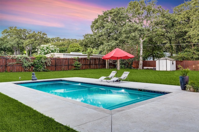 pool at dusk with a fenced in pool, a lawn, a fenced backyard, an outbuilding, and a storage unit