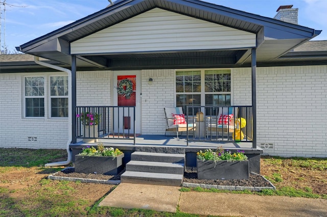 view of front of property featuring a porch, a chimney, brick siding, and crawl space