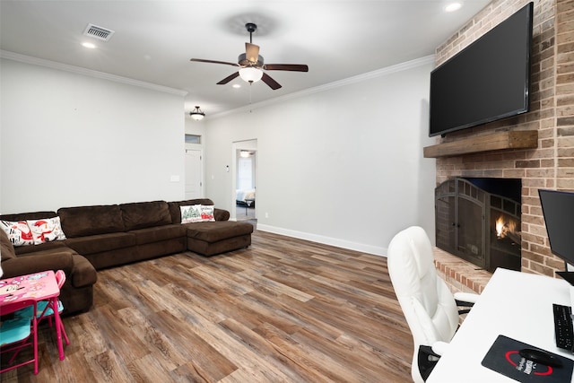 living area with visible vents, ornamental molding, wood finished floors, baseboards, and a brick fireplace