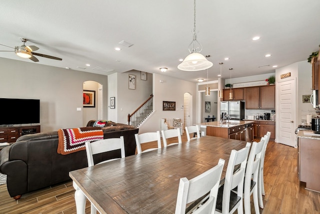 dining area featuring a ceiling fan, recessed lighting, arched walkways, light wood-style floors, and stairs