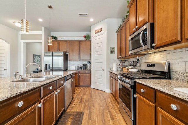 kitchen with visible vents, a sink, stainless steel appliances, light wood finished floors, and hanging light fixtures