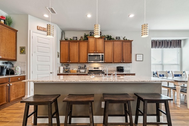 kitchen featuring visible vents, light wood-style flooring, a sink, stainless steel appliances, and brown cabinetry