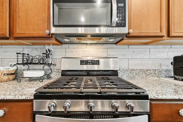 interior details with brown cabinetry, stainless steel appliances, light stone counters, and decorative backsplash