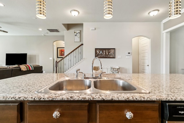 kitchen featuring open floor plan, light stone counters, dishwashing machine, arched walkways, and a sink