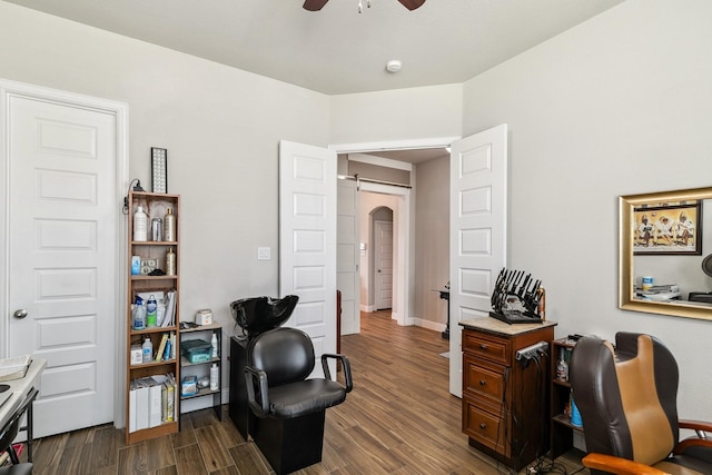 home office featuring dark wood finished floors, a barn door, arched walkways, baseboards, and ceiling fan