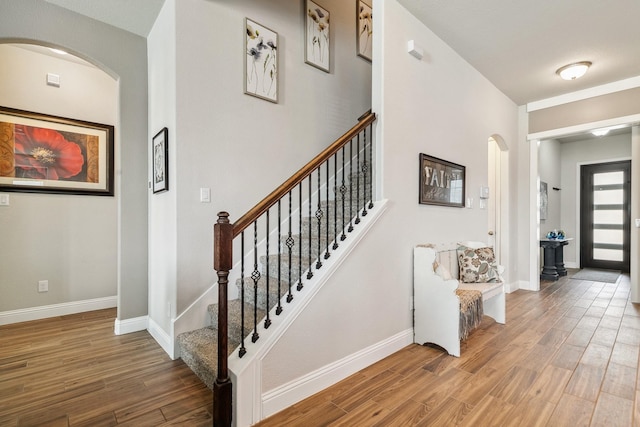 stairway featuring baseboards, arched walkways, and wood finished floors