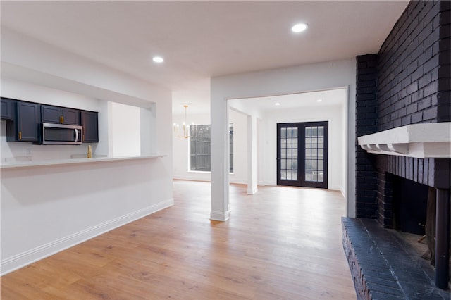 unfurnished living room featuring light wood-style flooring, a fireplace, baseboards, and french doors