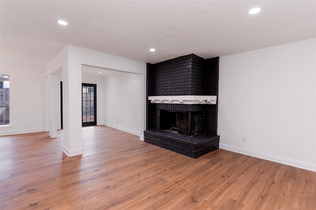 unfurnished living room featuring a brick fireplace, recessed lighting, wood finished floors, and baseboards