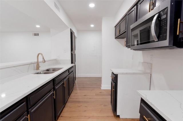 kitchen featuring visible vents, light wood-type flooring, a sink, stainless steel microwave, and light stone countertops