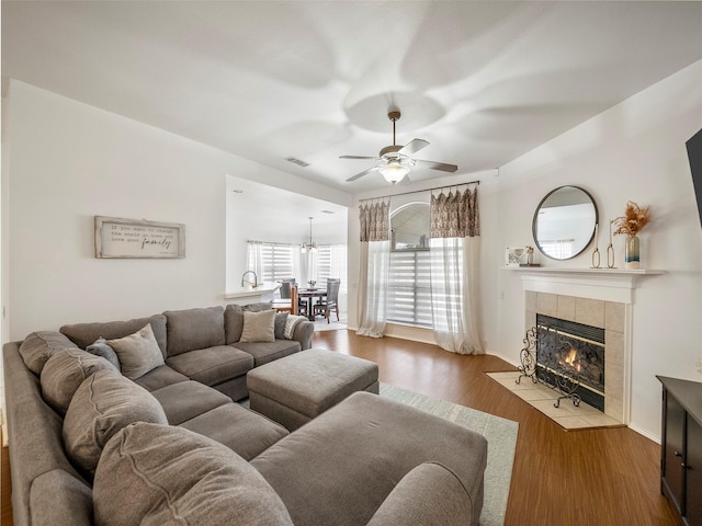 living room with a ceiling fan, a tile fireplace, and wood finished floors