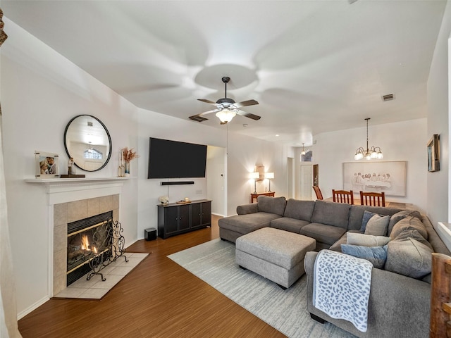 living room featuring visible vents, wood finished floors, a tiled fireplace, and ceiling fan with notable chandelier