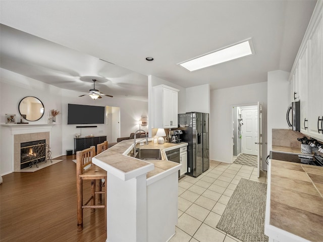 kitchen with a sink, black fridge, stainless steel microwave, a breakfast bar, and white cabinets