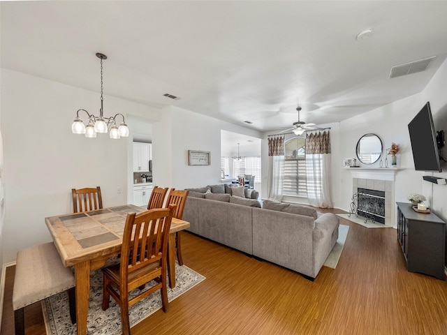 dining space with a chandelier, a fireplace, light wood-style flooring, and a ceiling fan