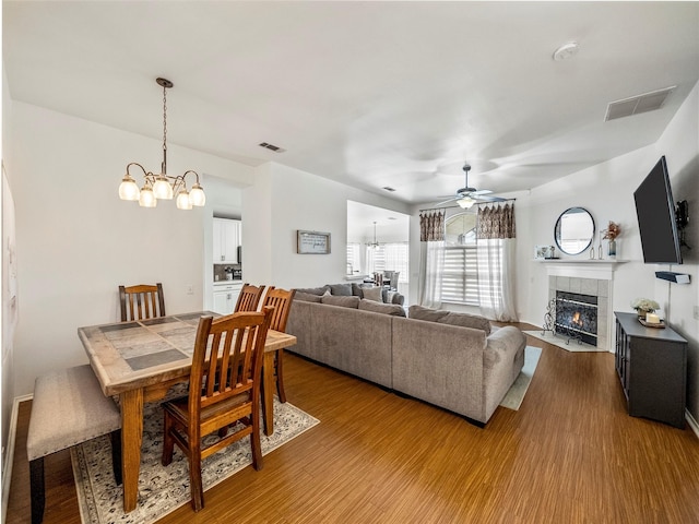 dining area featuring a chandelier, a tiled fireplace, wood finished floors, and ceiling fan