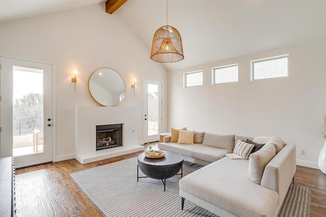 living area with beam ceiling, high vaulted ceiling, a fireplace with raised hearth, wood finished floors, and baseboards