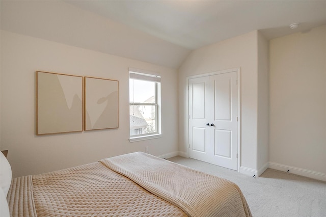 bedroom with lofted ceiling, baseboards, a closet, and light carpet