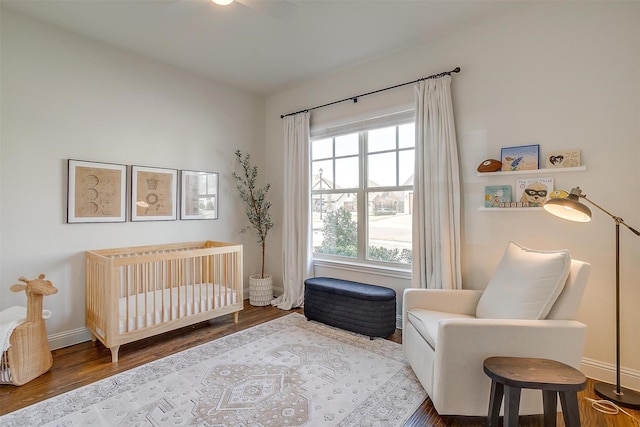 bedroom featuring baseboards, a nursery area, and wood finished floors