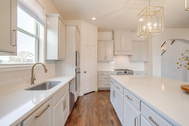 kitchen featuring a sink, light countertops, custom range hood, appliances with stainless steel finishes, and pendant lighting