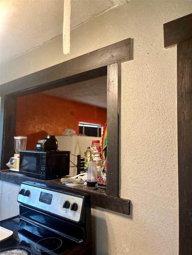 room details with stainless steel electric range, black microwave, and a textured wall