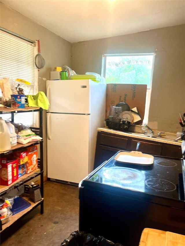 kitchen with unfinished concrete floors, black range with electric stovetop, and freestanding refrigerator