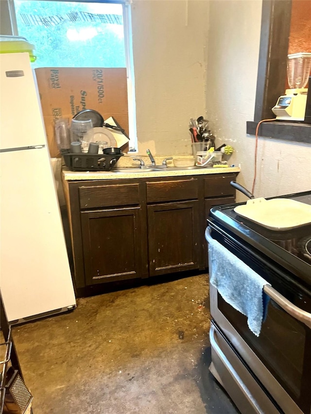 kitchen with freestanding refrigerator, stainless steel range with electric cooktop, light countertops, dark brown cabinets, and unfinished concrete floors