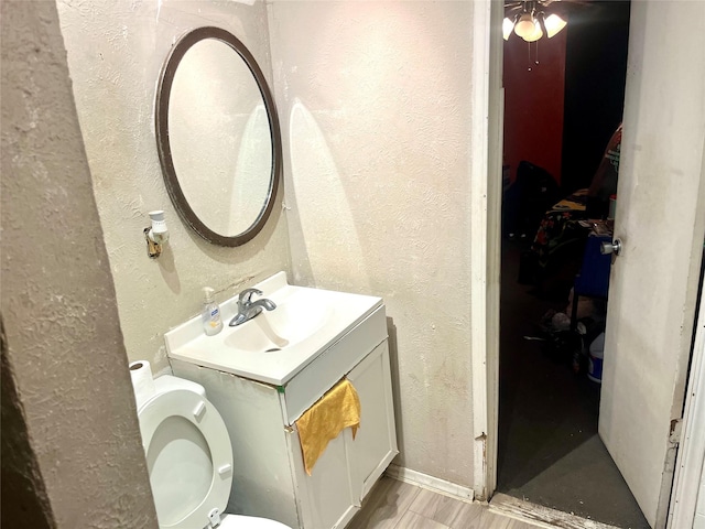 half bath featuring vanity, wood finished floors, toilet, and a textured wall