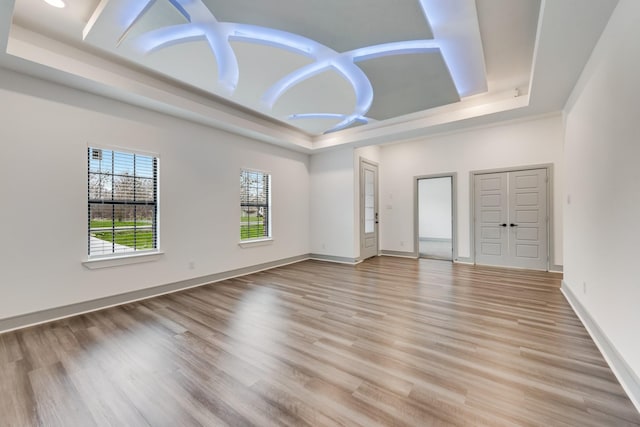 spare room featuring a tray ceiling, light wood-style flooring, and baseboards