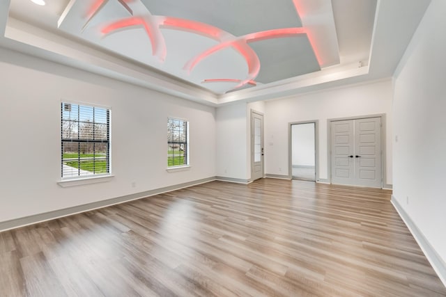 empty room featuring a raised ceiling, baseboards, and light wood finished floors