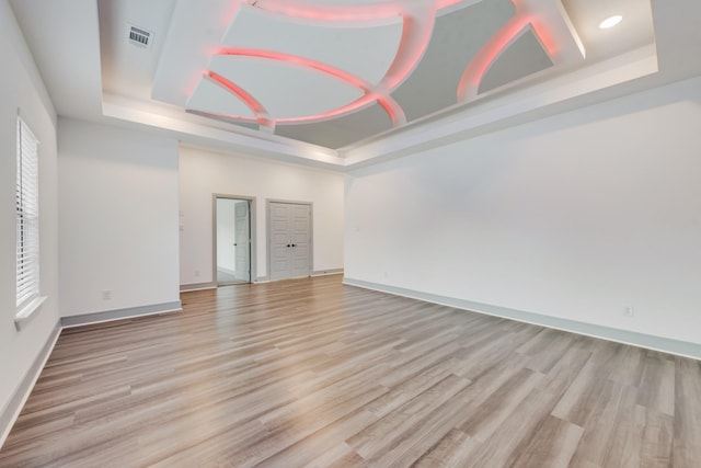 spare room featuring a tray ceiling, baseboards, light wood-style floors, and visible vents